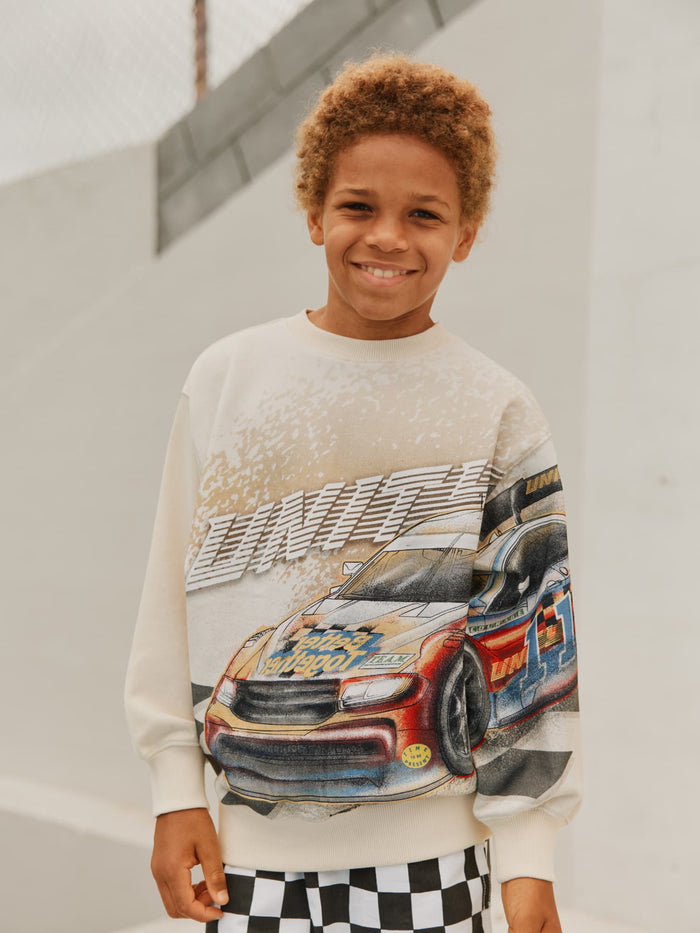 Child wearing a sweater with a car graphic on a plain background