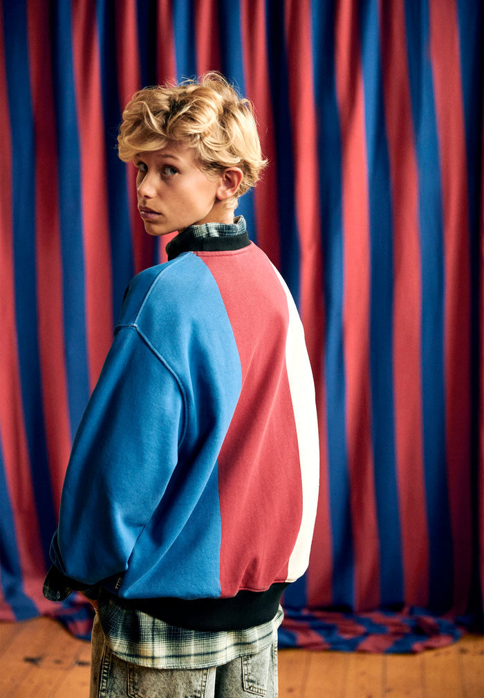 Person wearing a blue and red sweatshirt in front of a red and blue striped curtain
