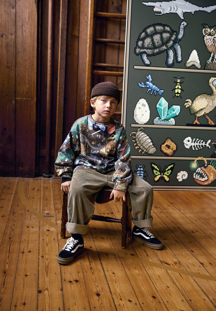 Child sitting on a chair in front of a chalkboard with educational drawings.