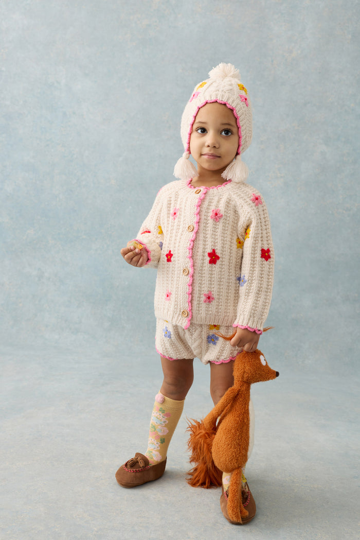 Child wearing a knitted outfit with colorful patterns, standing against a light blue background.