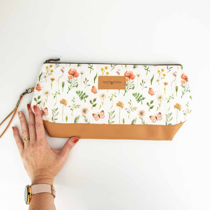 Mountain Meadow Trinity Bag styled on a wooden tray with a knitting project in progress, row counter chain, and a candle nearby