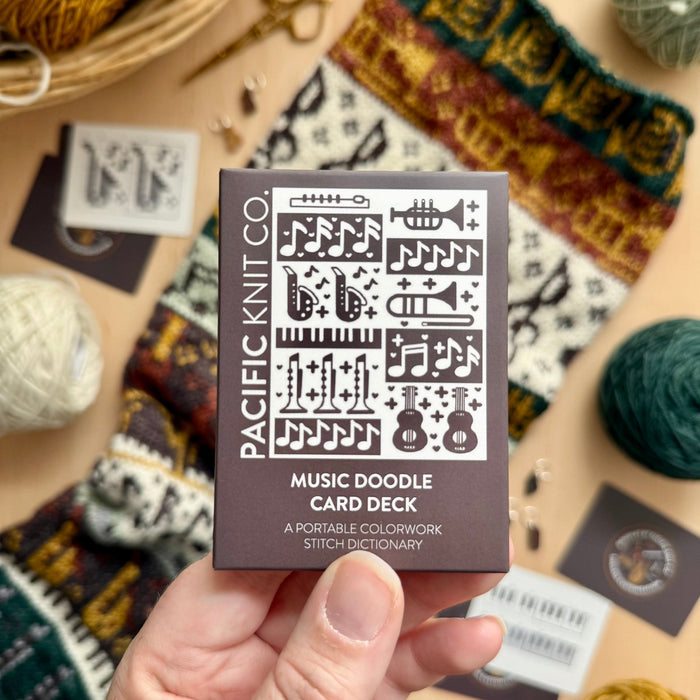 Hand holding the brown Music Doodle Card Deck by Pacific Knit Co tuckbox