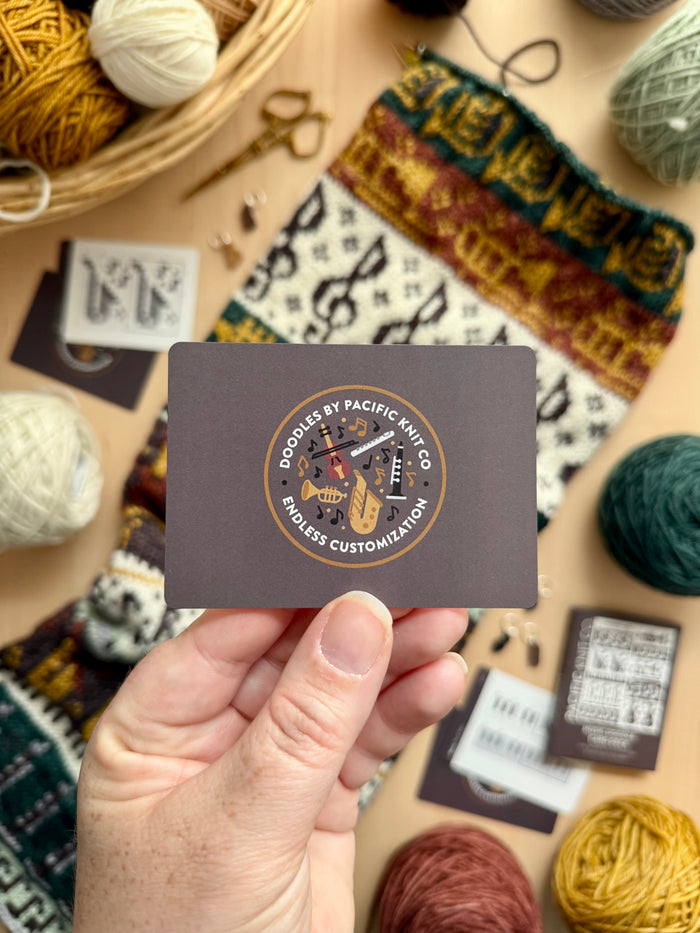 Hand holding the brown Pacific Knit Co card back with the Doodles logo
