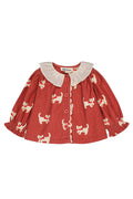 A toddler's long-sleeve button-up blouse in terracotta red with a cream-colored cat print and a cream ruffled Peter Pan collar, shown flat on a white background.