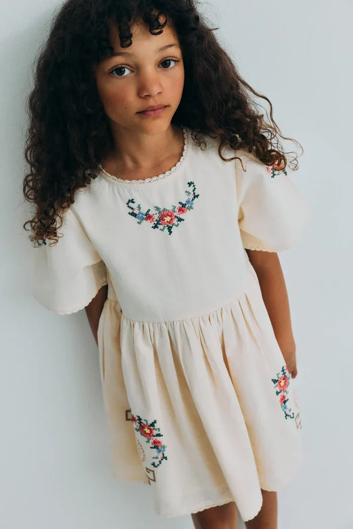 Young girl wearing a white dress with floral embroidery against a plain background