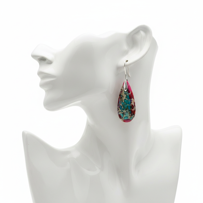 A pair of statement dangle earrings featuring large teardrop-shaped stones with a vibrant, marbled pattern of pink, blue, cream, and tan. Each stone is set in a thin gold-toned metal frame and hangs from a simple gold French hook. The earrings are displayed on a white mannequin head against a clean, neutral background.
