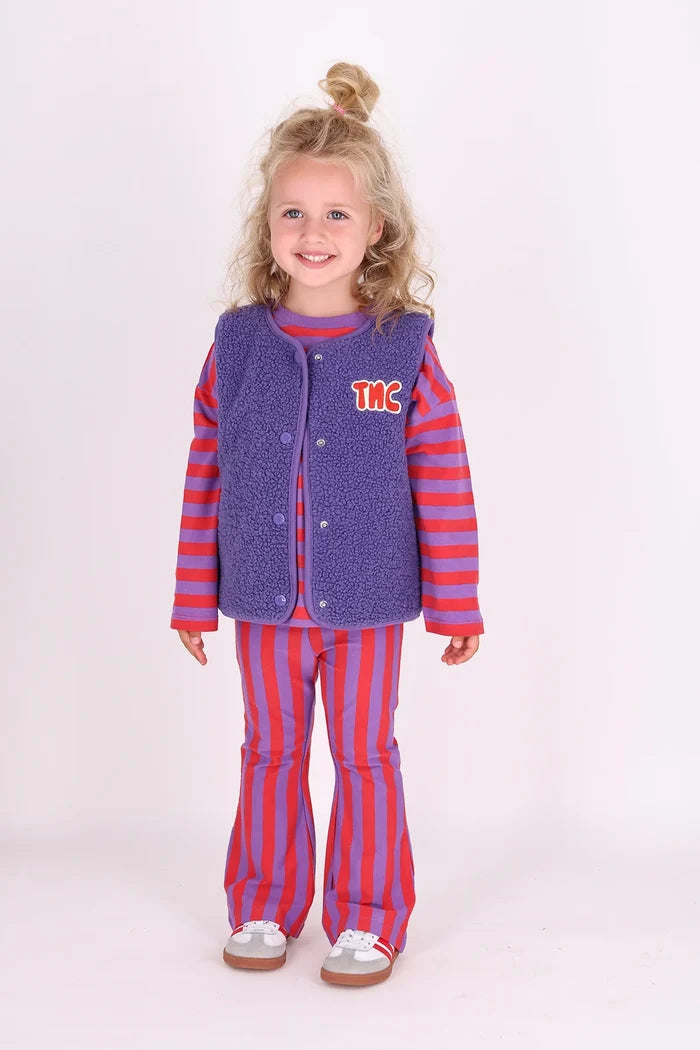 child wearing purple and red stripe flared leggings with matching striped top and purple sherpa vest on white background