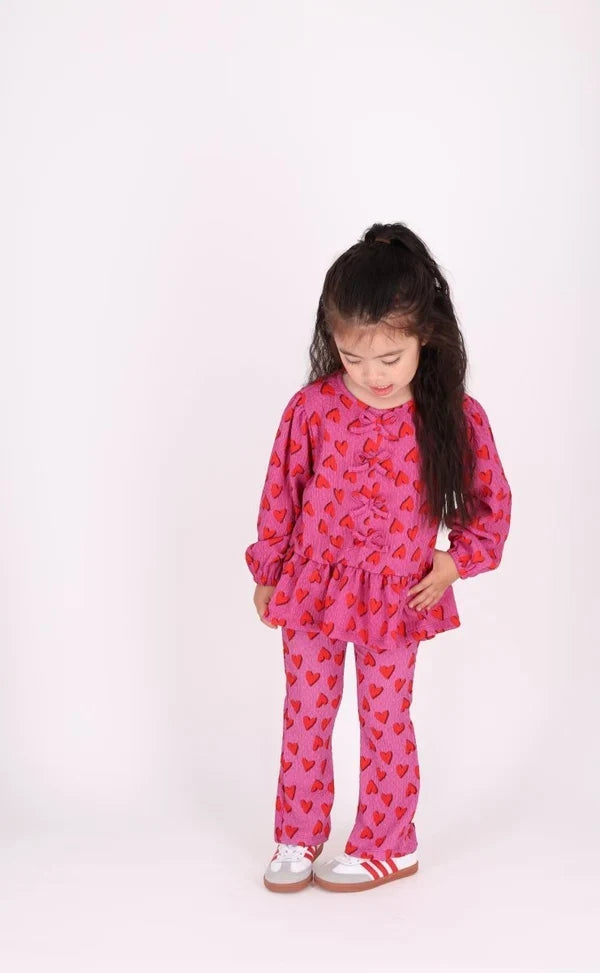 child wearing fuchsia flared leggings with red hearts all over and matching blouse on white background