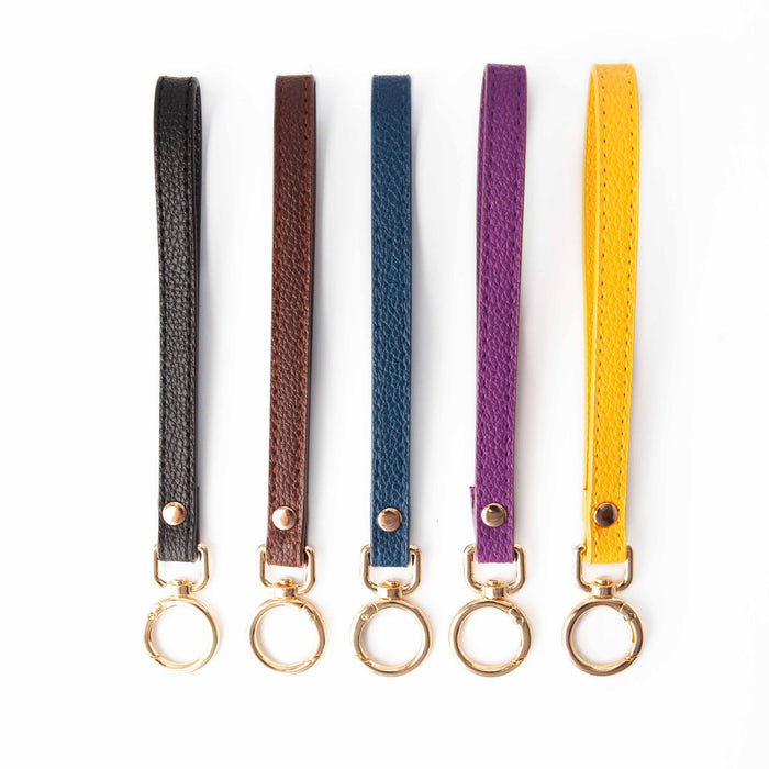 Five Wide Ring Yarn To Go Carousel wrist straps in black, brown, navy, plum, and mustard with gold spring ring clasps laid out side by side