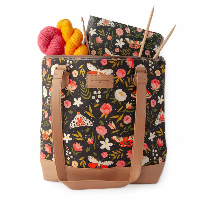Night Forest Mega Trinity Bag open from above showing yarn skeins in pink and golden yellow, bamboo knitting needles, and a matching Night Forest project journal planner inside