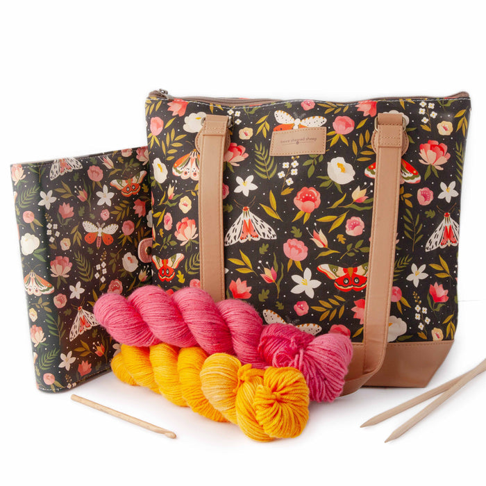 Night Forest Mega Trinity Bag styled with a matching Night Forest project journal planner, pink and golden yellow yarn skeins, bamboo knitting needles, and a crochet hook arranged in front