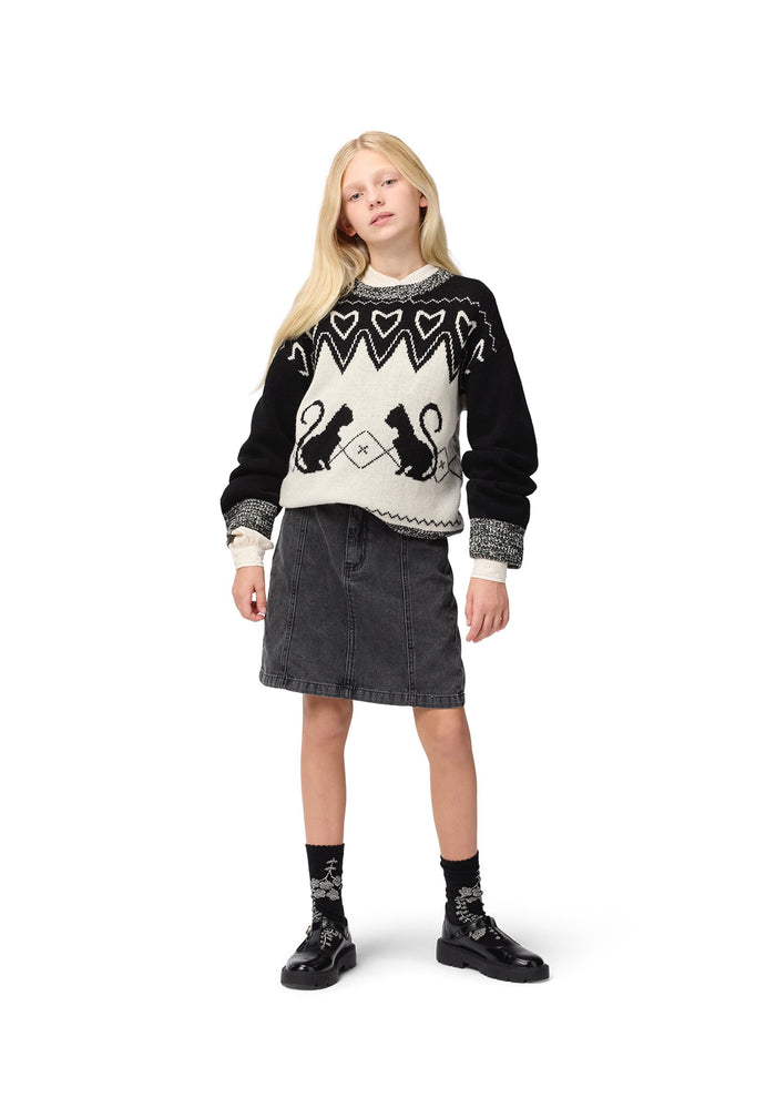 Young girl wearing a black and white sweater with cat designs on a white background