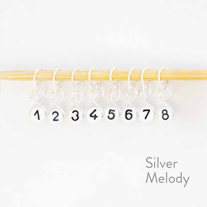 Silver melody clip style numbered stitch markers 1 through 8 with number beads hanging from bamboo knitting needle