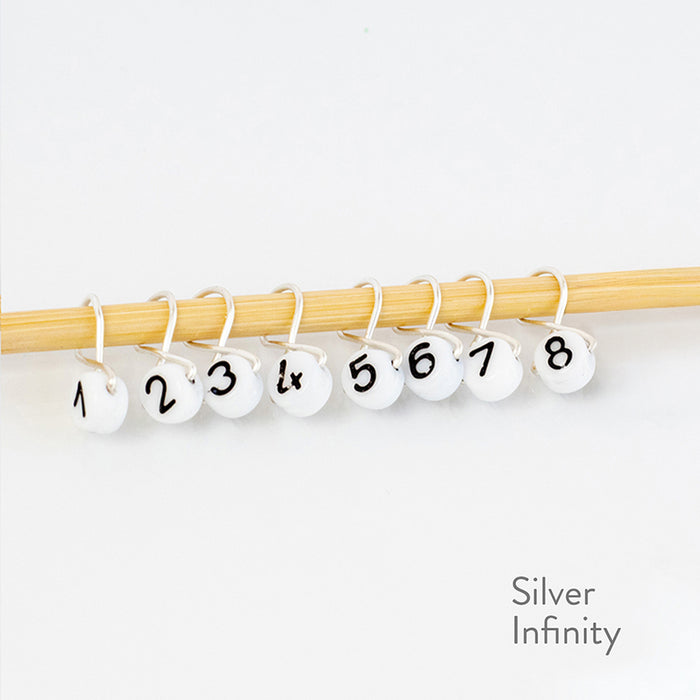 Silver infinity ring style numbered stitch markers 1 through 8 with number beads on bamboo knitting needle