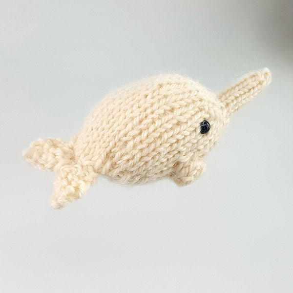Small cream hand-knit narwhal amigurumi toy with horn, black eye, and curled tail