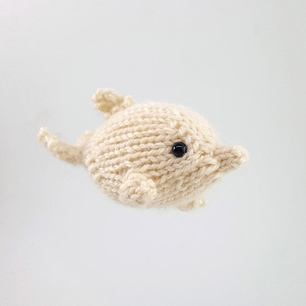 Small cream hand-knit dolphin amigurumi toy with black eye and fin detail