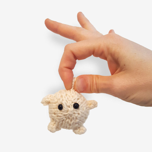 Hand holding tiny knitted cream puffer fish toy between two fingers from Ocean Buddies pattern