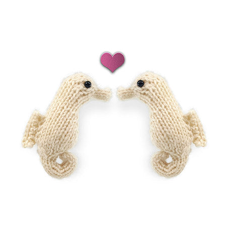 Two cream knitted seahorse toys facing each other with a small pink heart between them from the Ocean Buddies collection