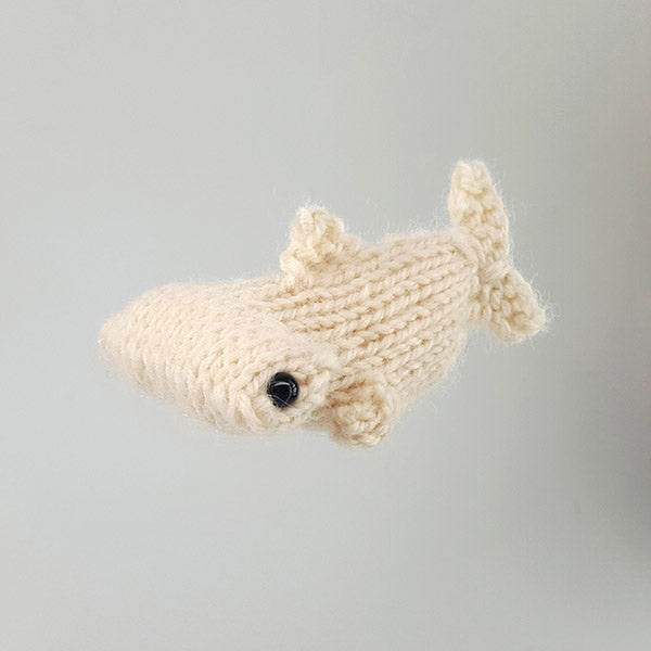 Small cream knitted hammerhead shark amigurumi toy viewed from the side on white background