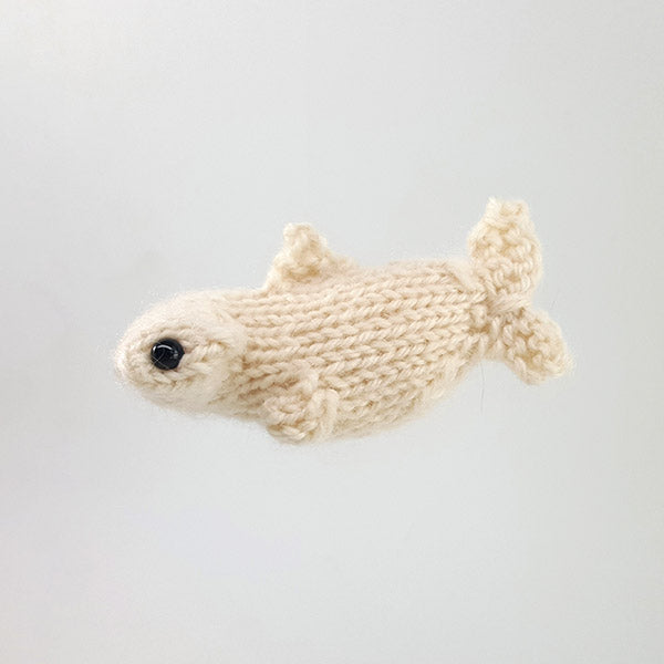 Cream knitted hammerhead shark toy with wide flat head, black bead eye, and small fins on gray background