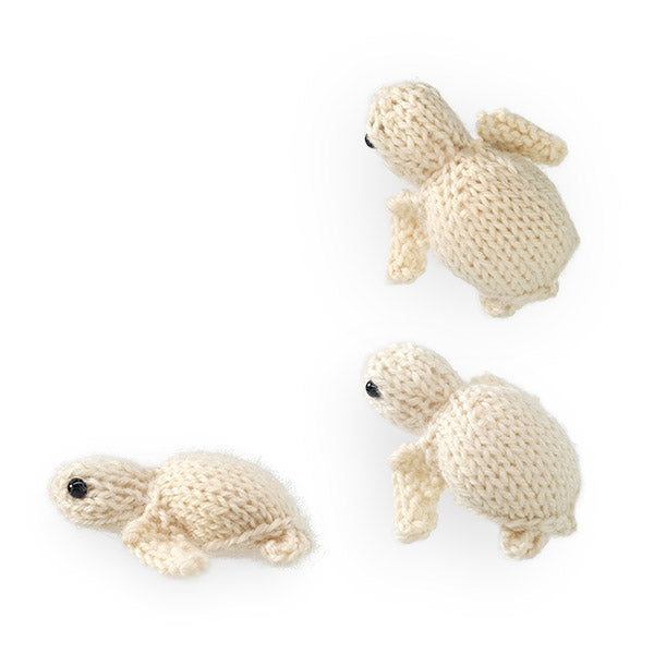 Three cream knitted sea turtles in different sizes arranged on white background, viewed from above