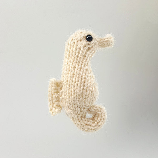 Small cream hand-knit seahorse amigurumi toy with black eye and curled tail