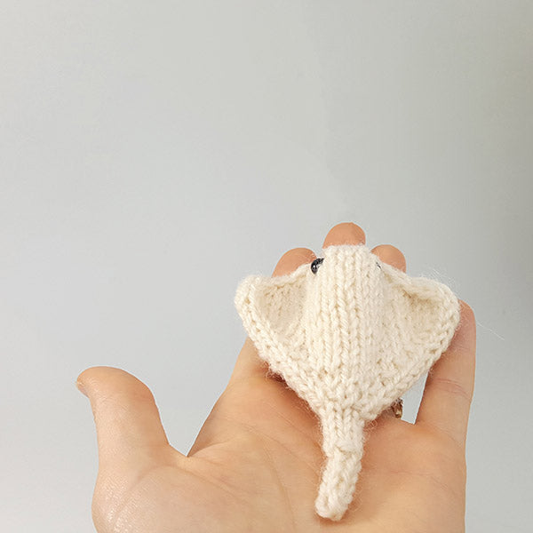 Small cream knitted stingray amigurumi toy held in palm showing flat body and tail