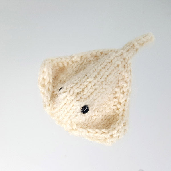 Small cream knitted stingray amigurumi toy with black bead eyes on white surface