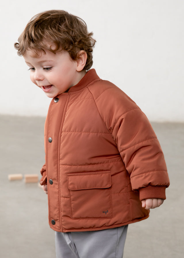 Child wearing a brown quilted jacket on a plain background