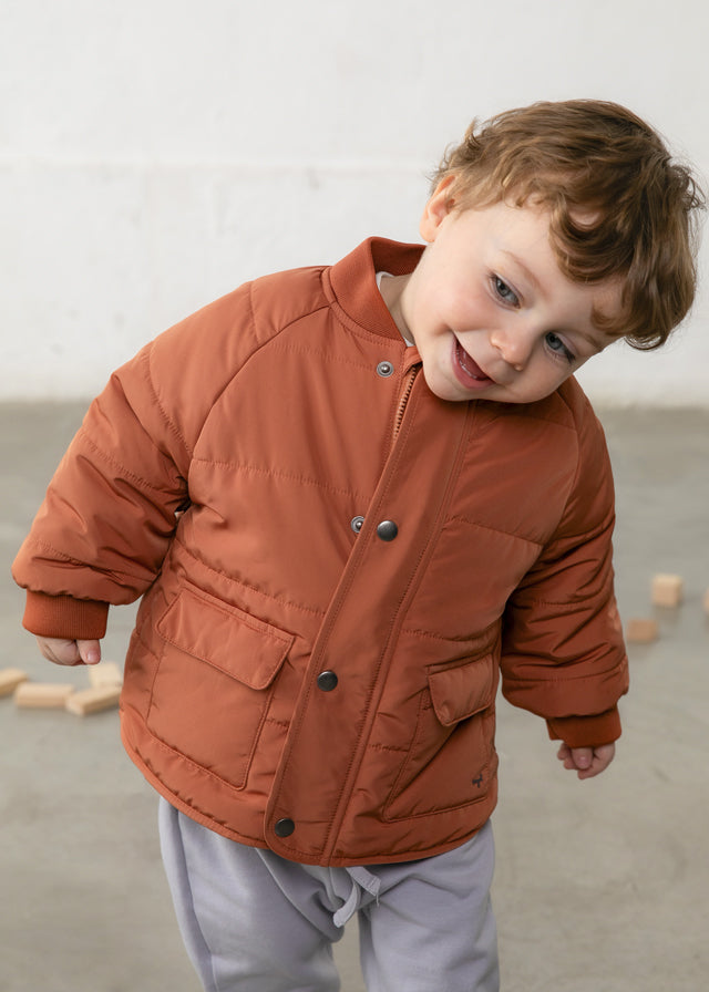 Child wearing a brown quilted jacket on a neutral background