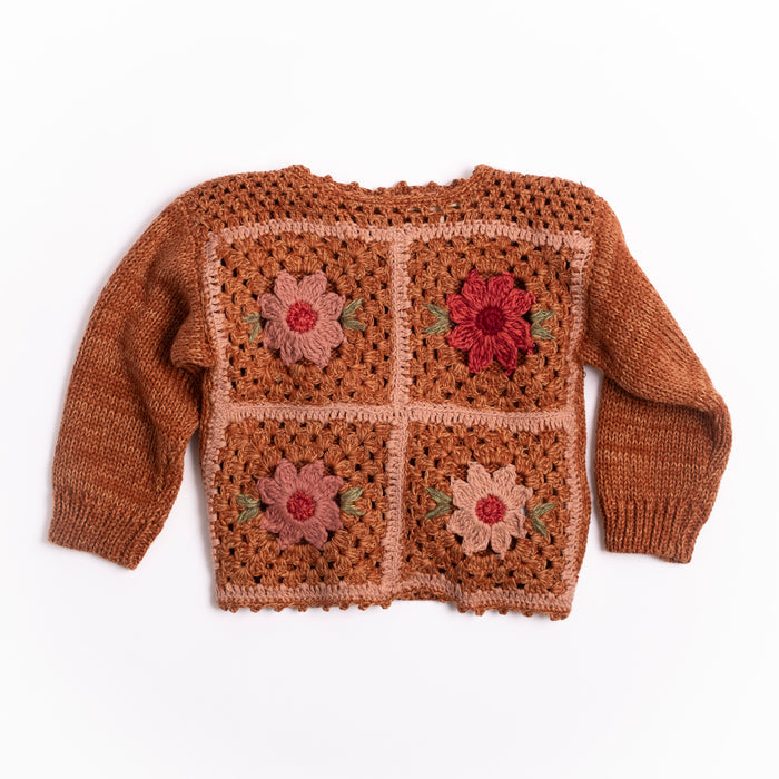 A brown crocheted knit sweater with four large floral panels on the front, featuring pink, red, and beige flowers with small green leaves, laid flat on a white background.
