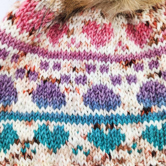 Close-up of colorwork pawprint pattern detail on knit beanie in pink, purple, and teal speckled yarn