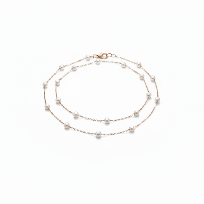A delicate 18k gold-dipped double-layer anklet featuring evenly spaced "floating" pearls on a fine titanium steel chain, captured in a minimalist editorial style for a refined summer aesthetic.