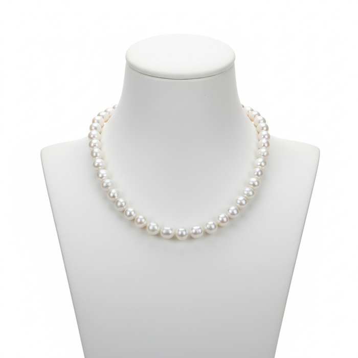 A classic strand of high-lustre, uniform white pearls displayed on a minimalist white bust, representing a foundational piece for a refined jewelry collection with a clean, editorial aesthetic.