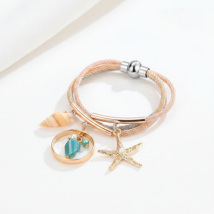 Multi-strand mesh bracelet in gold and silver tones featuring beach-inspired charms including a gold starfish, a seashell, and a teal gemstone drop, shown on a clean white surface with professional lighting.