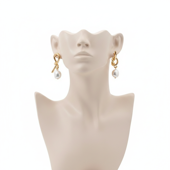 Elegant gold-toned knotted loop dangle earrings featuring large teardrop-shaped baroque pearls on a minimalist mannequin display.