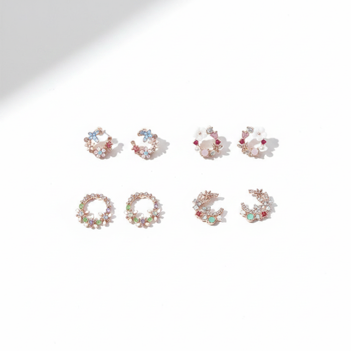 Four pairs of rose gold-tone stud earrings in delicate circular wreath and crescent shapes, featuring pastel blue, pink, and green gemstones with tiny floral accents on a bright white background.