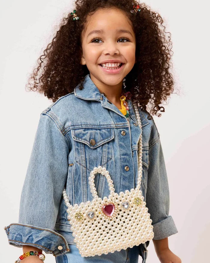 Child wearing a denim jacket holding a decorative white handbag with a heart charm on a light background
