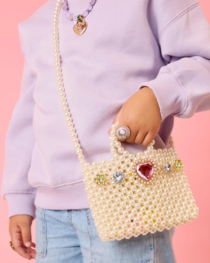 Person holding a pearl-handled handbag with decorative elements against a pink background