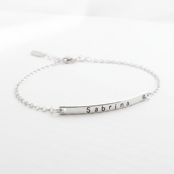 Minimalist silver chain bracelet with a curved bar engraved with the name Sabrina on a white background
