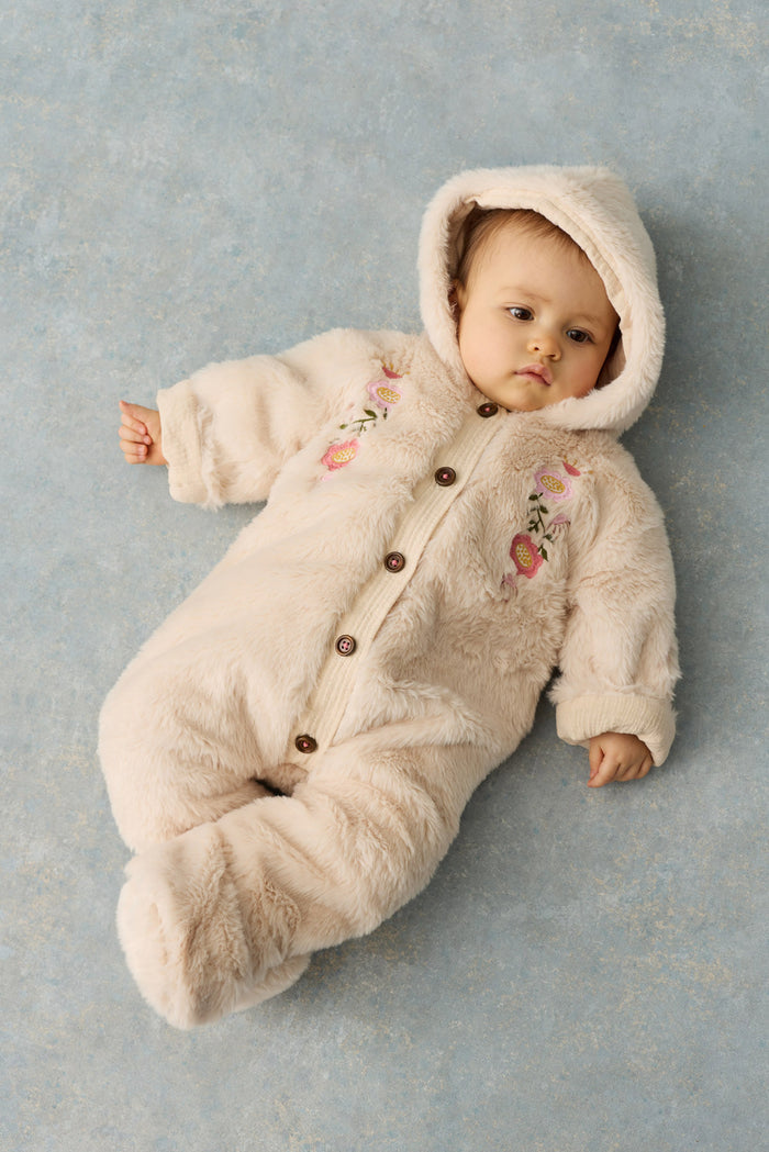 baby laying on grey background dressed in faux fur hooded romper with flroal embroidery on chest.