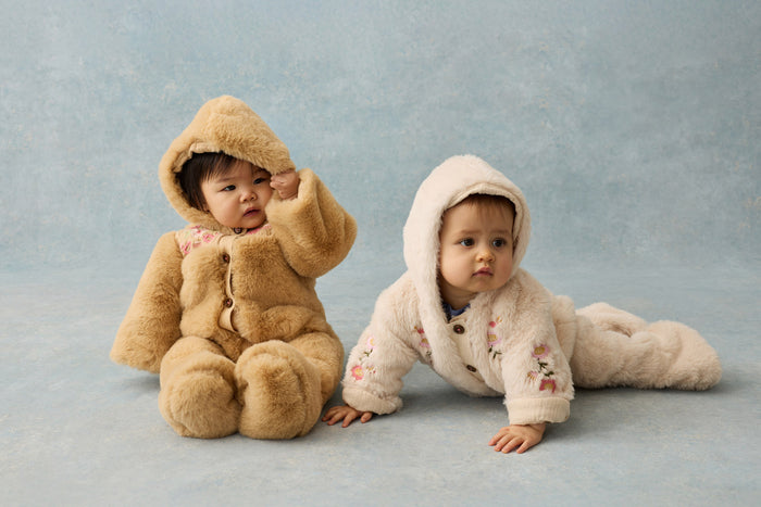 two babies wearing faux fur rompers on grey background.