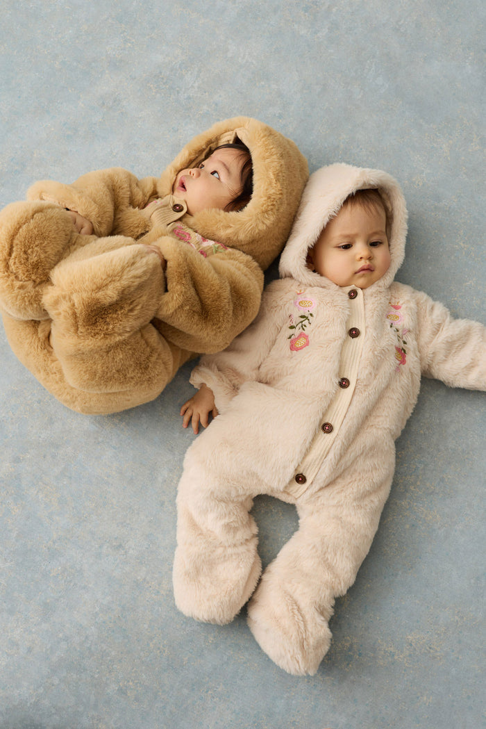 two babies in faux fur rompers laying on grey backdrop.