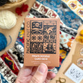 Hand holding the tan Pirate Doodle Card Deck by Pacific Knit Co tuckbox