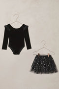 Black velvet bodysuit with sheer sleeves and black sequin skirt on hangers against a beige background