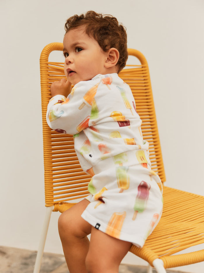 Child wearing a colorful outfit sitting on a yellow chair against a plain background
