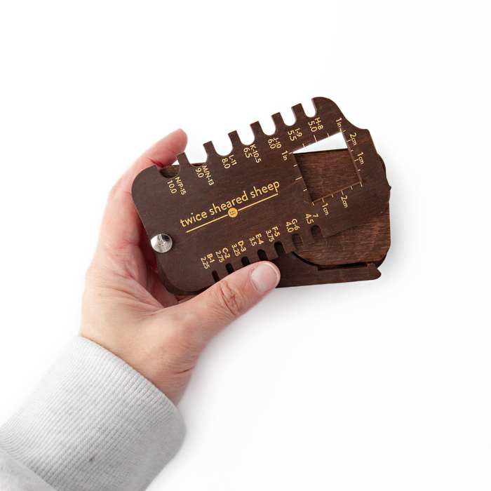 Hand holding the Stitch Scout Multi-Tool unfolded to show the needle gauge and gauge square