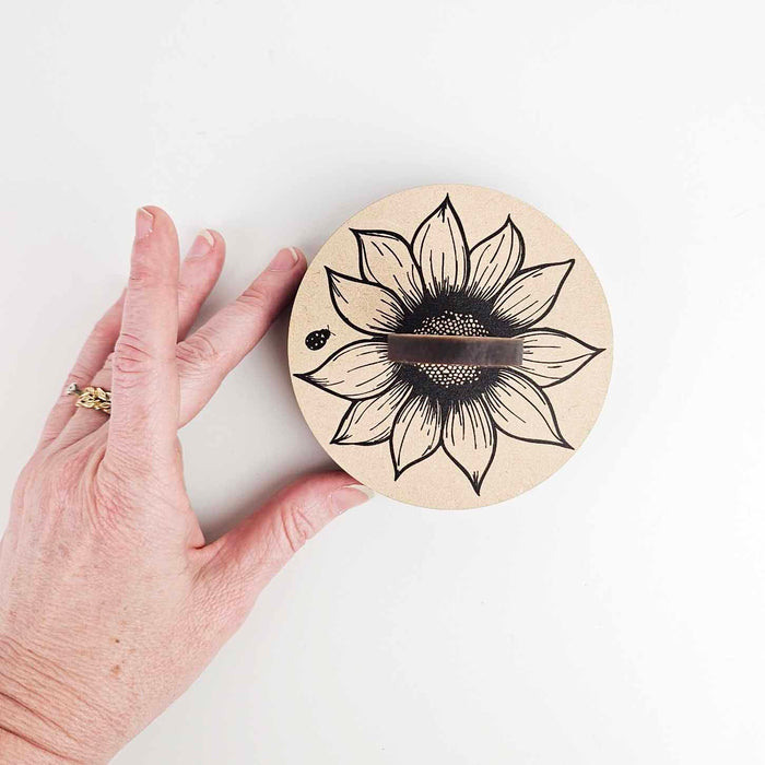 Hand holding Sunflower Yarn To Go Carousel wooden base plate showing sunflower and ladybug design with yarn slot