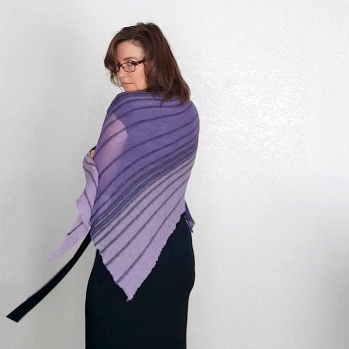 Back view of model wearing the Primus shawl in gradient purple with horizontal ridged stripes, draped across her shoulders over a black dress