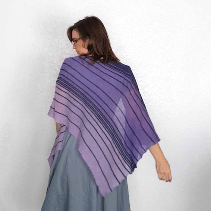 Back view of model wearing the Primus shawl in gradient purple and lavender with dark horizontal stripes, spread wide across her shoulders over a gray skirt